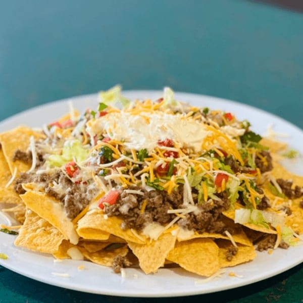 A plate of DON PIBIL GRILL nachos with ground beef, cheese, lettuce, tomatoes, and sour cream.
