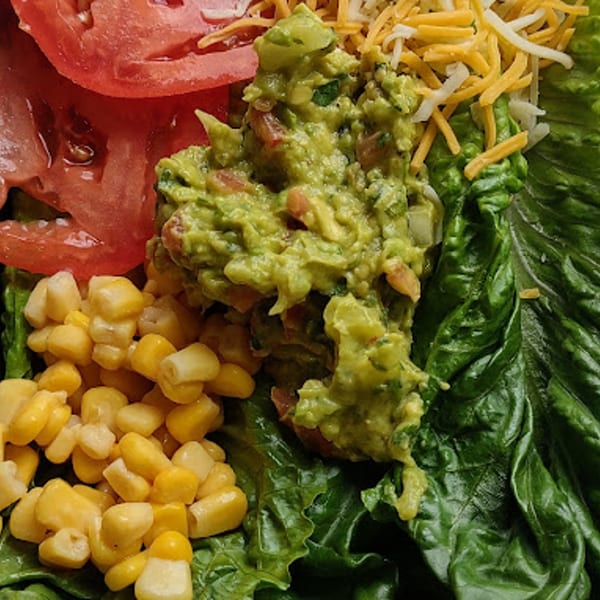 Close-up of a vibrant Mexican salad with guacamole, corn, tomatoes, and shredded cheese on lettuce.