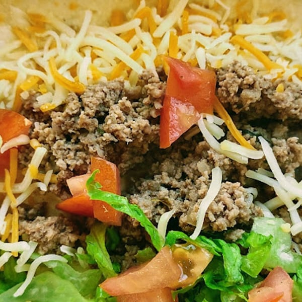 Close-up of a taco with seasoned ground beef, shredded cheese, diced tomatoes, and lettuce.